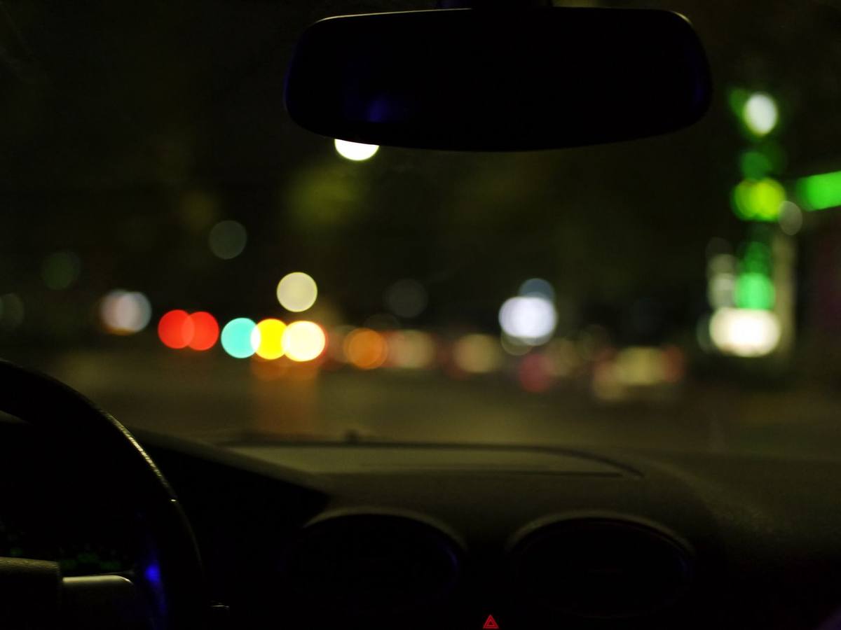 Vista de dentro de um carro à noite, com as luzes da rua desfocadas